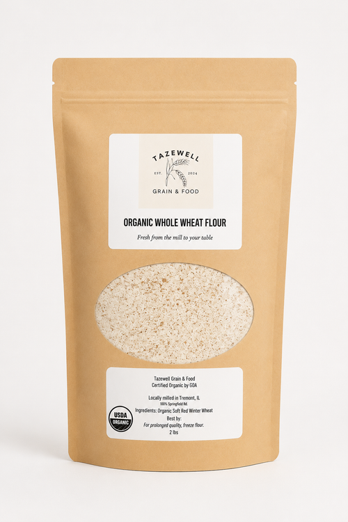 A stand-up brown paper bag of Tazwell Grain & Food Organic Whole Wheat Flour, featuring a white label and a clear window showing the flour inside, set against a plain light background.